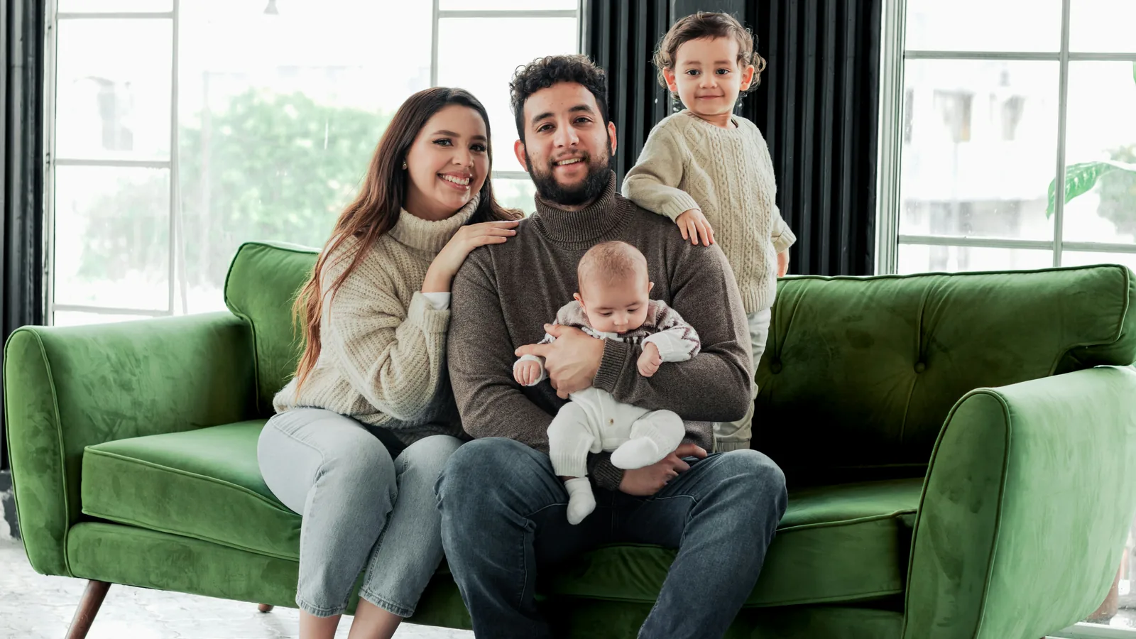 A smiling couple on a green sofa with a baby and a toddler.